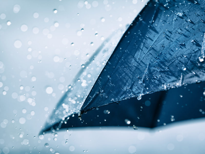 Blue umbrella under heavy rain against cloudy sky background. Rainy weather concept.