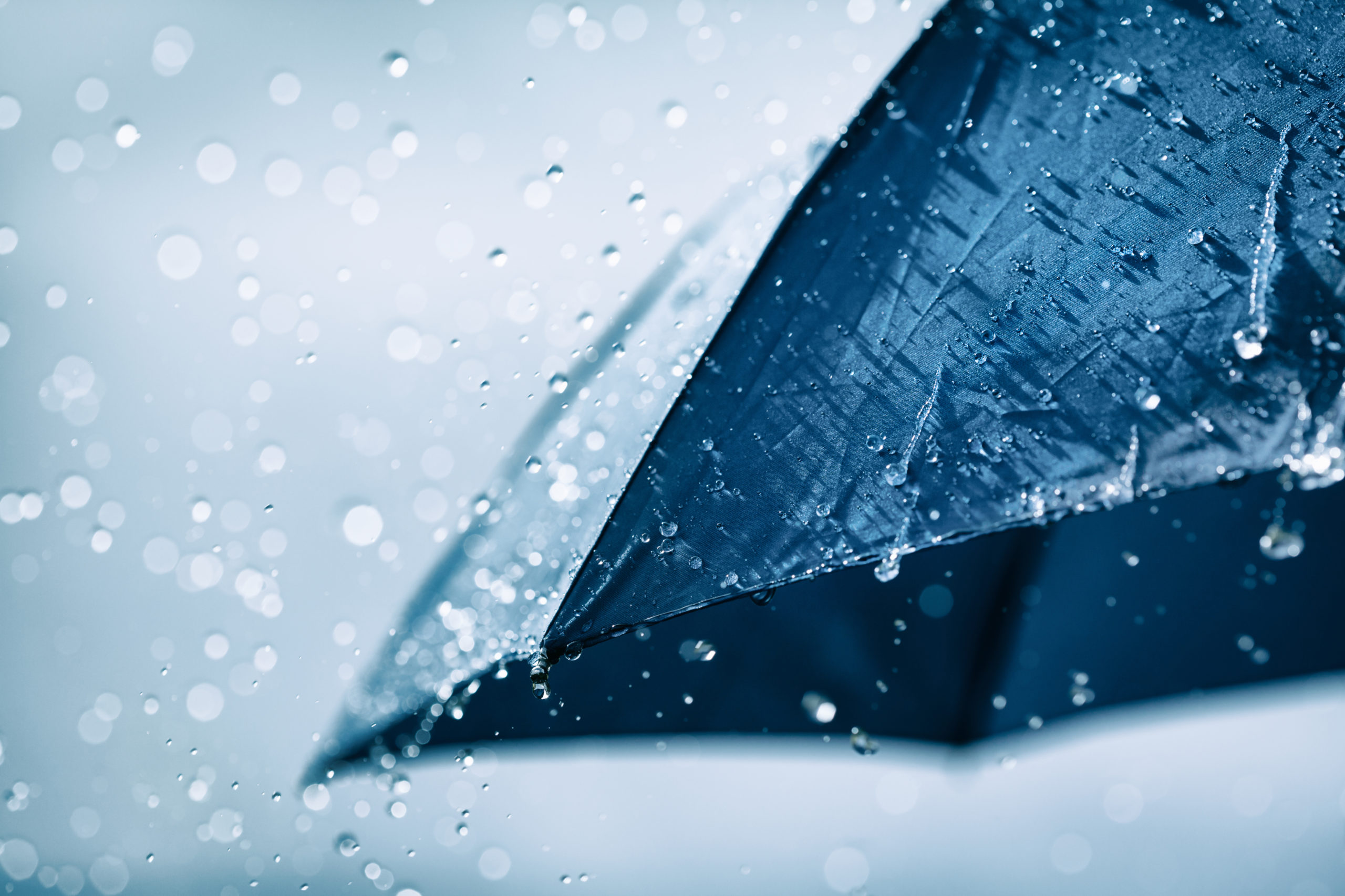 Blue umbrella under heavy rain against cloudy sky background. Rainy weather concept.