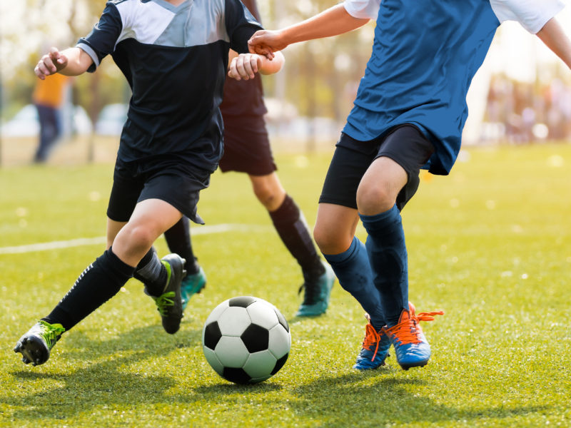 Two soccer players running and kicking a soccer ball. Legs of two young football players on a match. European football youth player legs in action