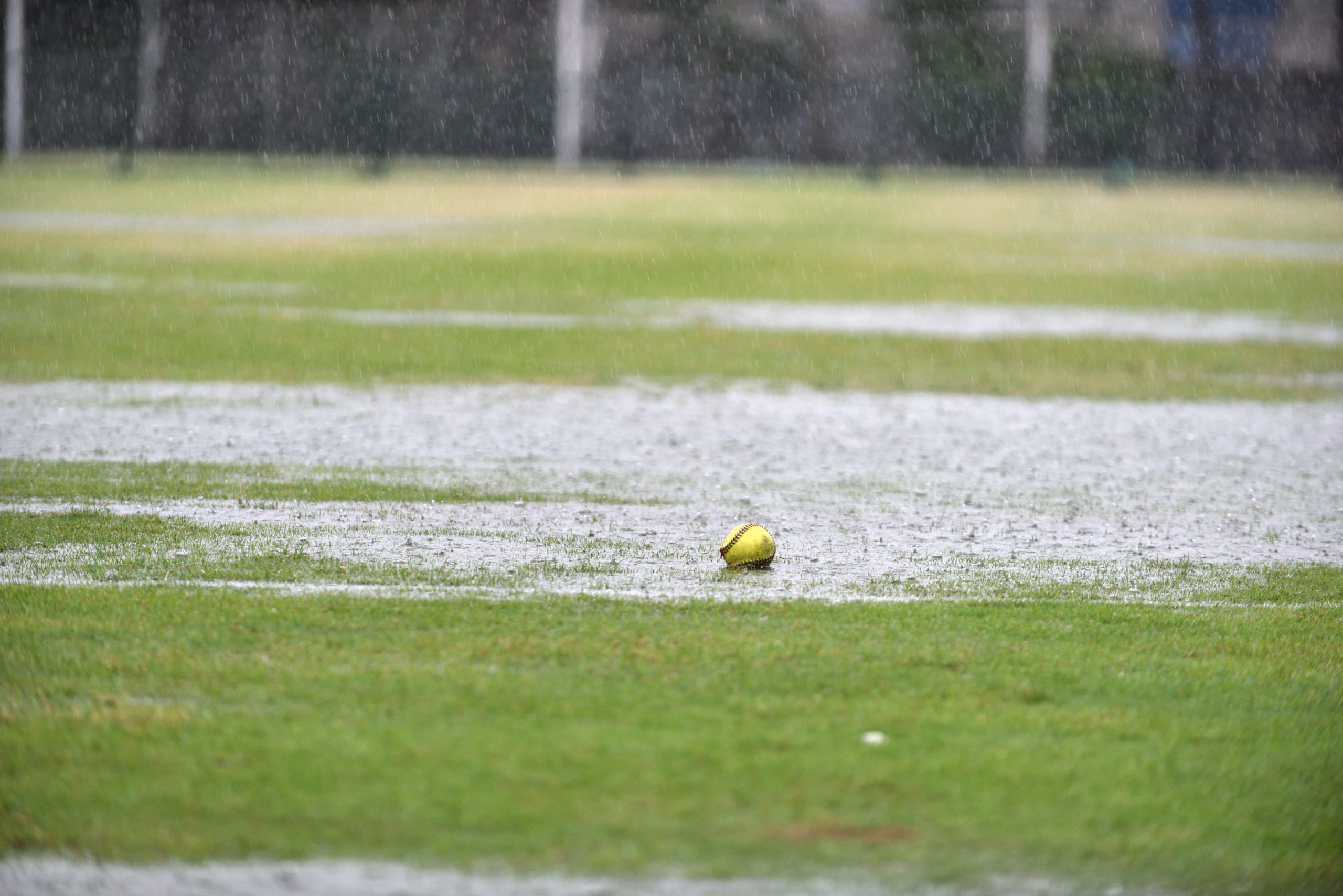 A fresh green softball left on a raining field waiting for a league match to begin while the field is full with water and no player.
